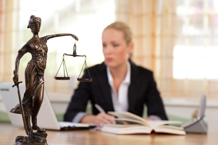 Bild - Eine Referendarin am Schreibtisch beim Studium und im Vordergrund auf dem Tisch die Justitia. Das Bild zeigt eine Referendarin am Schreibtisch beim Studium und auf dem Tisch im Vordergrund die Justitia (die Personifikation der Gerechtigkeit) ist das Symbol der Gerichtsbarkeit. Ihre Waage ist ein Sinnbild für das Abwägen von Standpunkten und das Zumessen der Strafe. Ihr Buch symbolisiert das Gesetz und das Schwert dessen Durchsetzung.