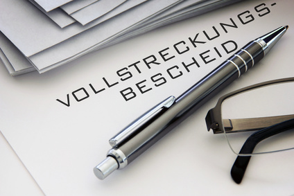 Das Bild zeigt einen Vollstreckungsbescheid mit Kugelschreiber und Teil einer Brille.