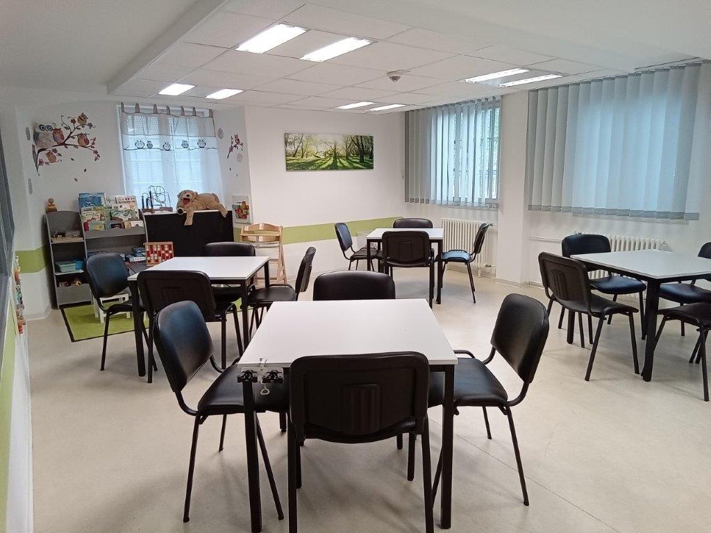 Besuchsraum mit vier Tischen mit Stühlen. Im Hintergrund eine Kinderspielecke.